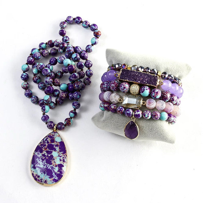 Purple beaded necklace with a teardrop pendant and matching bracelets on a white background