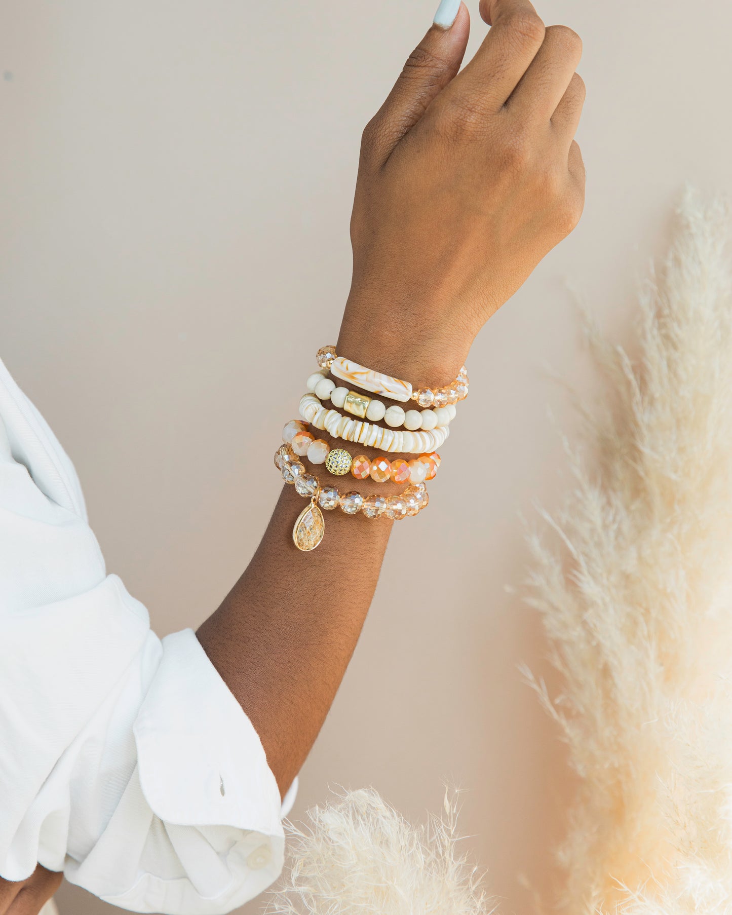 Hand wearing multiple pearl bracelets on a neutral background