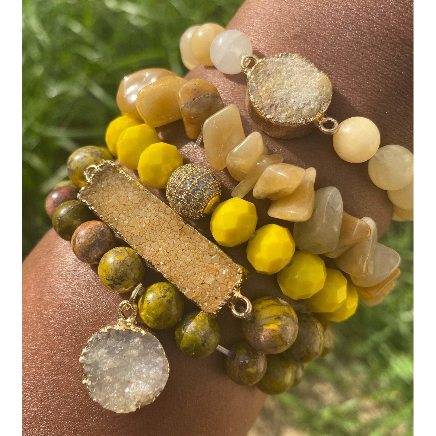 Multicolored beaded bracelet with gold accents on a wrist against a grassy background