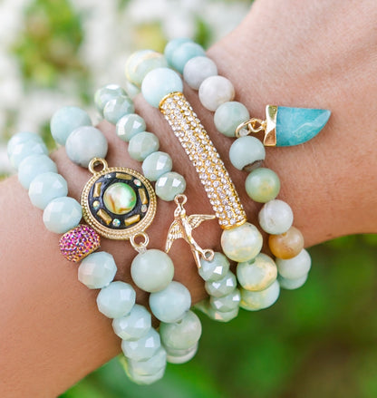 Multiple bracelets with beads and charms on a wrist against a blurred natural background