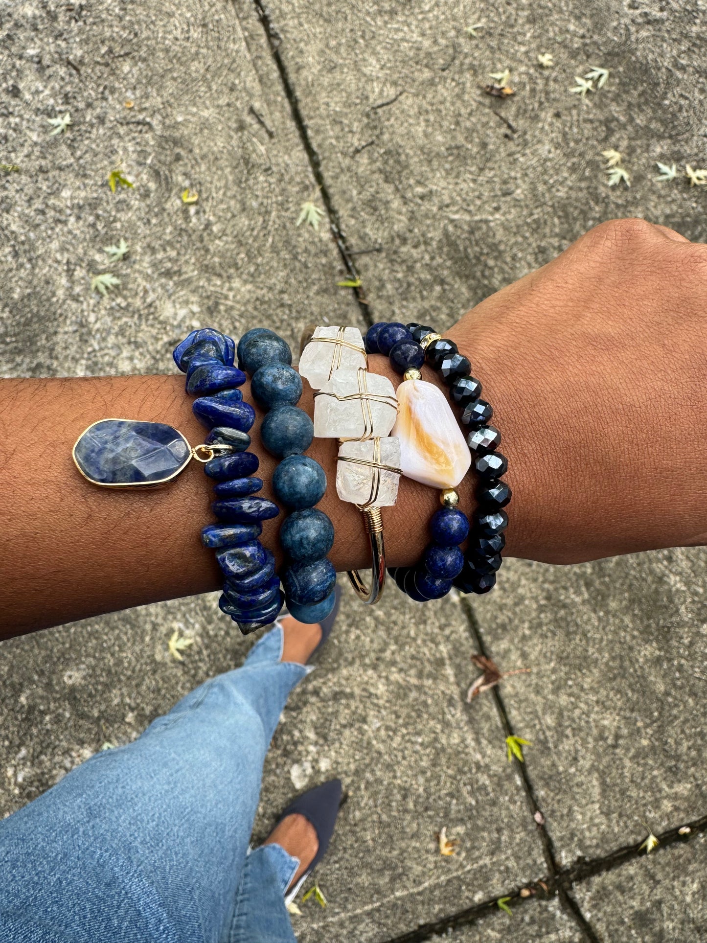 Hand wearing multiple blue beaded bracelets on a concrete surface