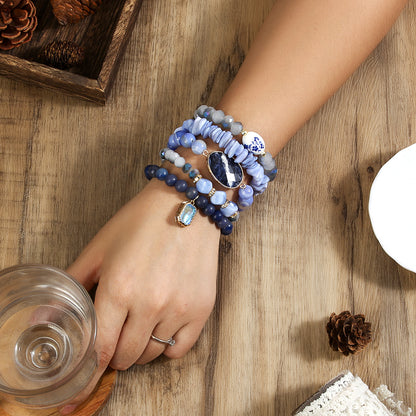 Hand wearing multiple blue beaded bracelets on a wooden surface with a glass of water and pine cones.