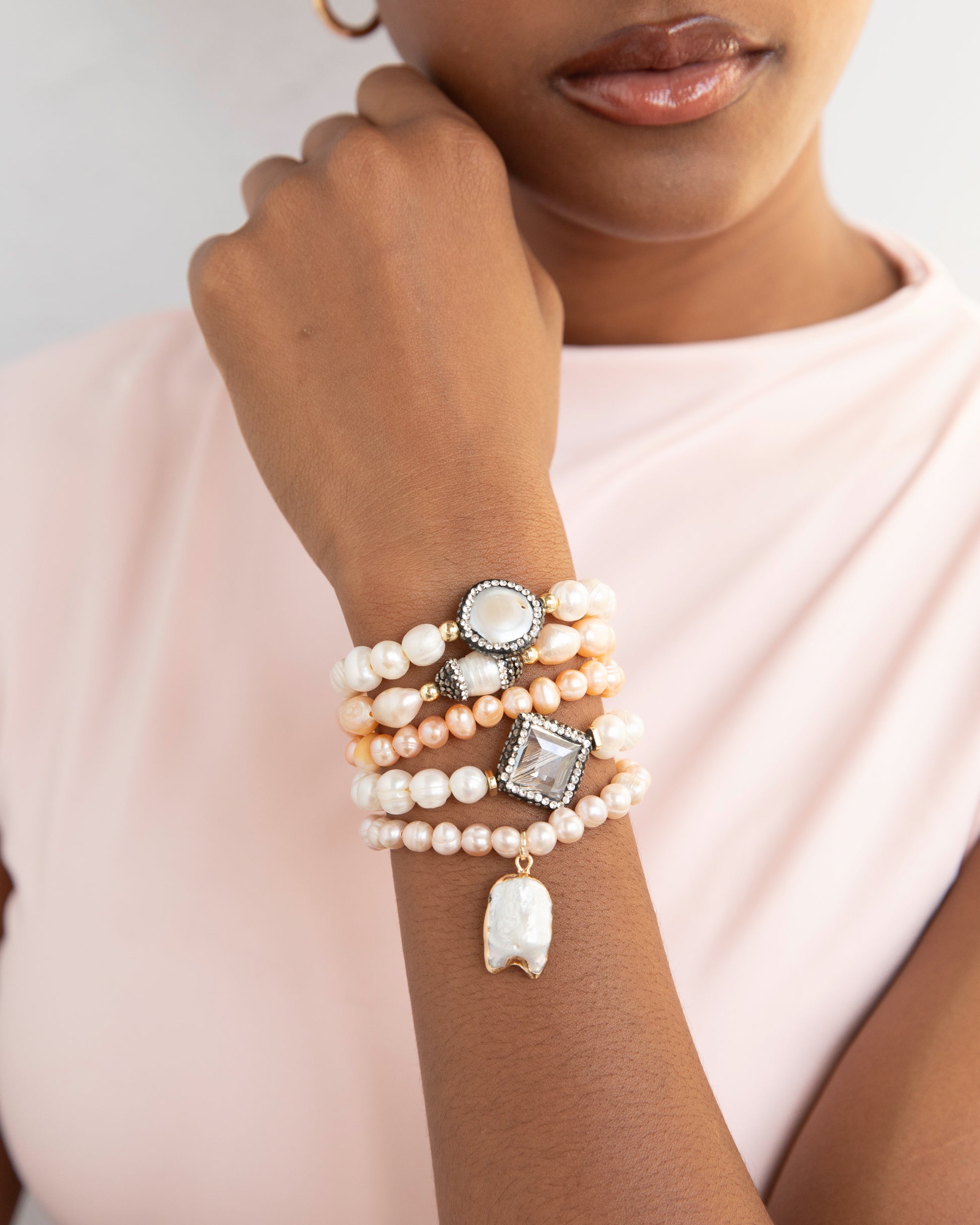 Woman wearing a stack of pearl bracelets on her wrist against a neutral background