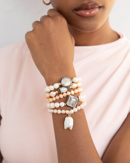 Woman wearing a stack of pearl bracelets on her wrist against a neutral background
