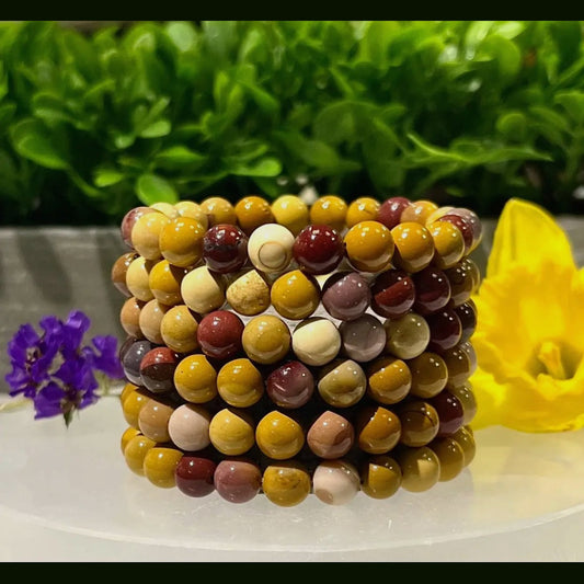 Stack of multicolored beaded bracelets on a white surface with greenery in the background
