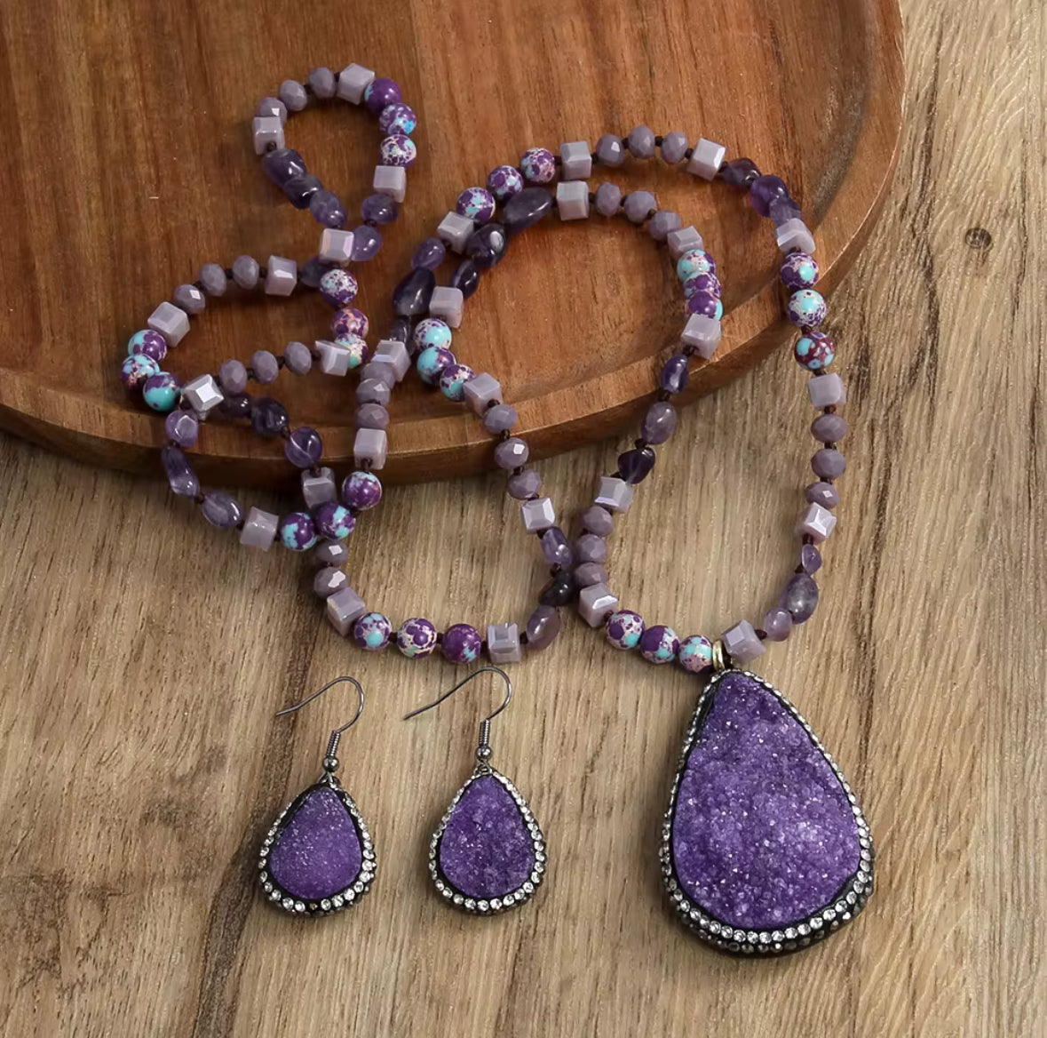 Purple beaded jewelry set including necklace, earrings, and pendant on a wooden surface