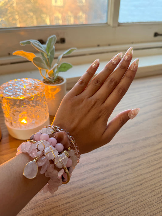 Hand wearing a pink bracelet with a blurred background of a plant and light.