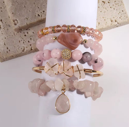 Stack of pink and gold beaded bracelets on a white surface with a stone background