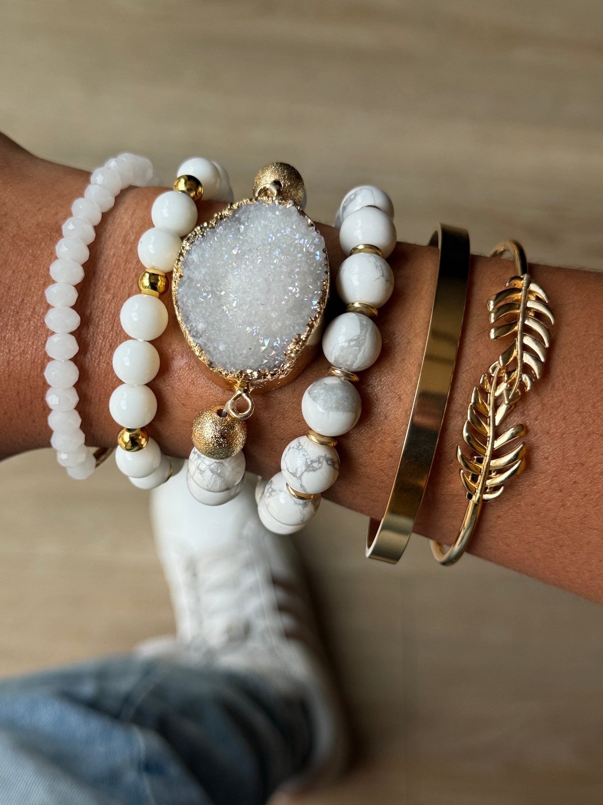 Close-up of a wrist wearing multiple gold and white bracelets