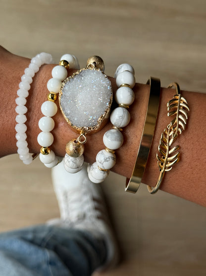 Close-up of a wrist wearing multiple gold and white bracelets