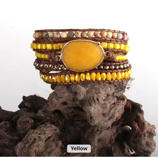 Multistrand bracelet with yellow beads and a large yellow stone on a textured surface.