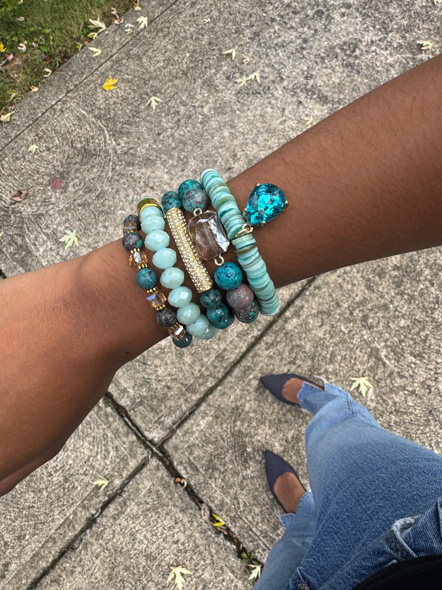 Close-up of a wrist wearing multiple turquoise beaded bracelets on a pavement background