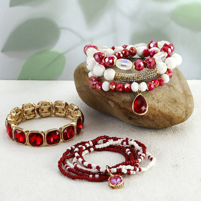 Jewelry set with red and white beaded bracelets on a stone surface with a blurred green leaf background.