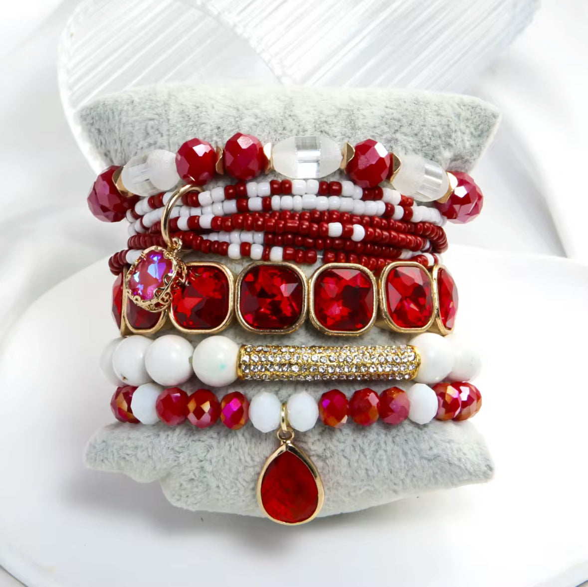 Stack of red and white beaded bracelets on a textured white surface