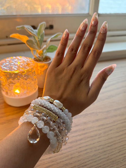 Hand wearing multiple bracelets with a blurred background of a plant and light source