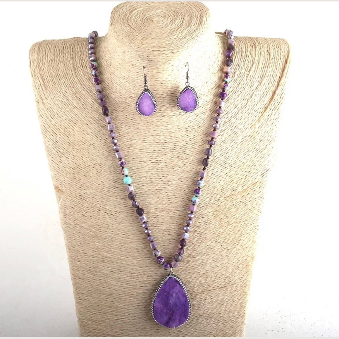 Purple beaded necklace and earrings on a beige mannequin bust.